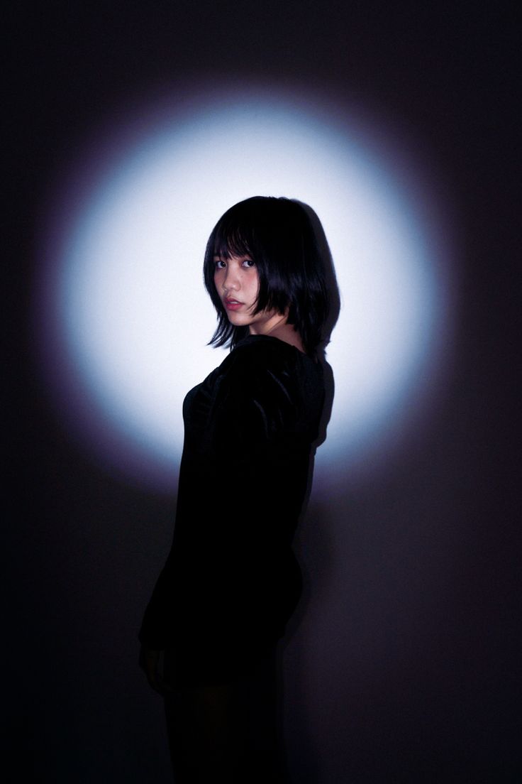 a woman with black hair standing in front of a white circle on a dark background