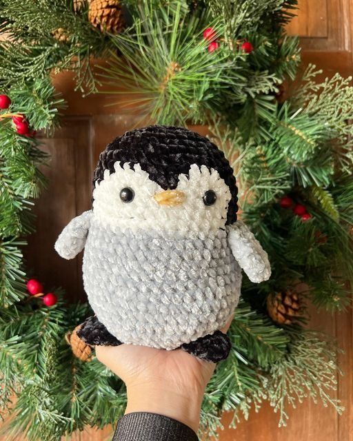 a hand holding a small penguin in front of a christmas wreath