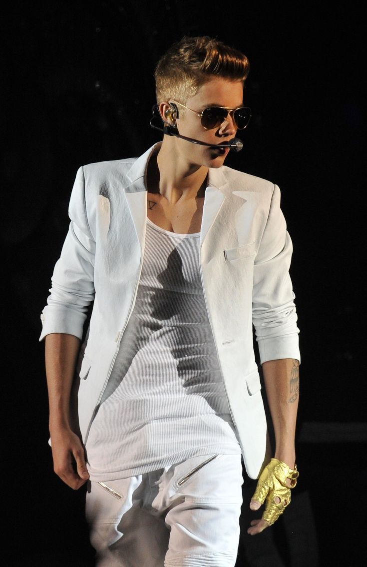 a male in a white suit and gold gloves on the runway at a fashion show