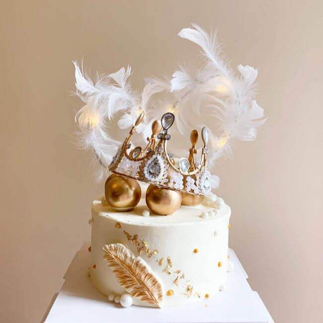 a white cake with gold decorations and feathers on top