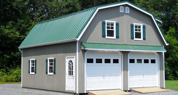 two garages with green roof and white doors on gravel road in front of trees