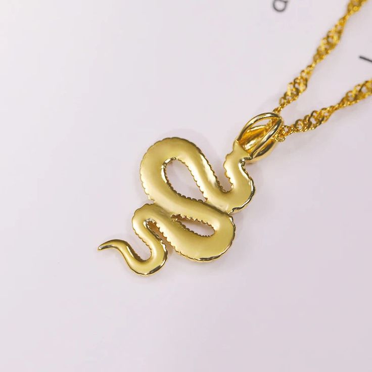 🐍 Embrace the allure of the serpent with our Year of the Snake Gold Necklace – a stunning piece that weaves elegance and symbolism into your everyday style! Available in both 18K gold over titanium steel, this necklace captures the essence of sophistication and durability. The sleek design features a captivating Singapore chain, offering versatility that allows you to wear it flat for a classic look or twisted for a contemporary twist. The 20-inch chain, complete with a 2-inch extension, ensure Snake-shaped Metal Necklace For Gift, Metal Snake Shape Necklace As Gift, Metal Snake-shaped Necklace For Gift, Gold Snake-shape Chain Jewelry, Gold Snake Shape Chain Jewelry, Yellow Gold Stainless Steel Snake Chain Jewelry, Metal Snake Chain Necklace For Gift, Snake Shape Gold Chain Necklace Gift, Gold Snake Shape Chain Necklace Gift