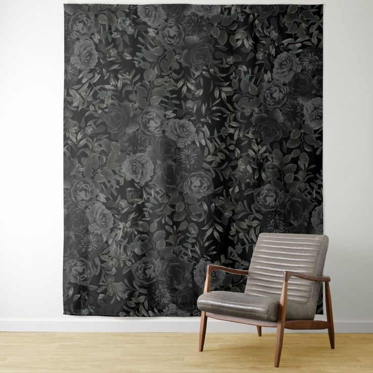 a chair sitting in front of a black floral wall hanging on a white wall next to a wooden floor