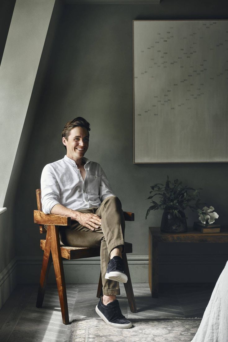 a man sitting in a chair with his legs crossed, smiling and looking at the camera