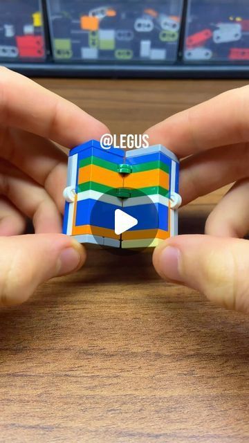 two hands holding an origami cube in front of a wooden table with cars on it