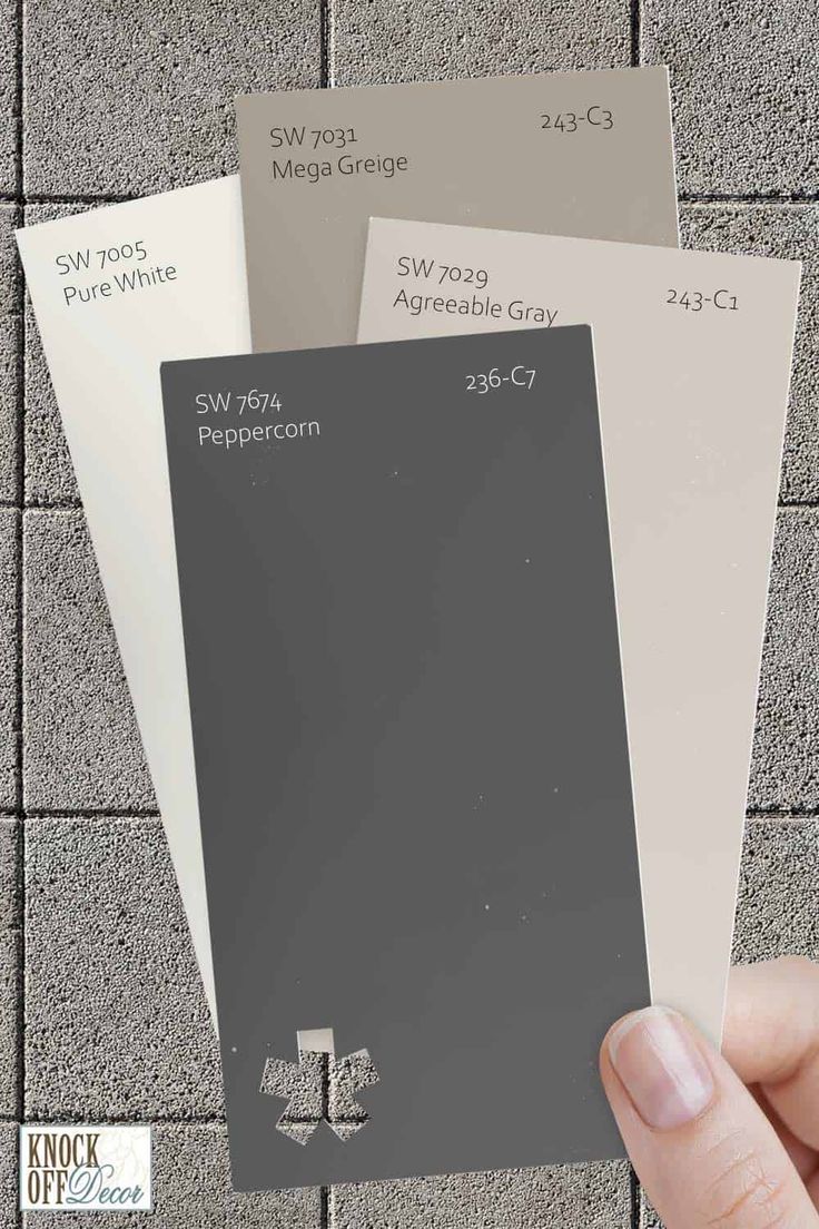 a hand holding three different shades of gray and white paint swatches in front of a brick wall