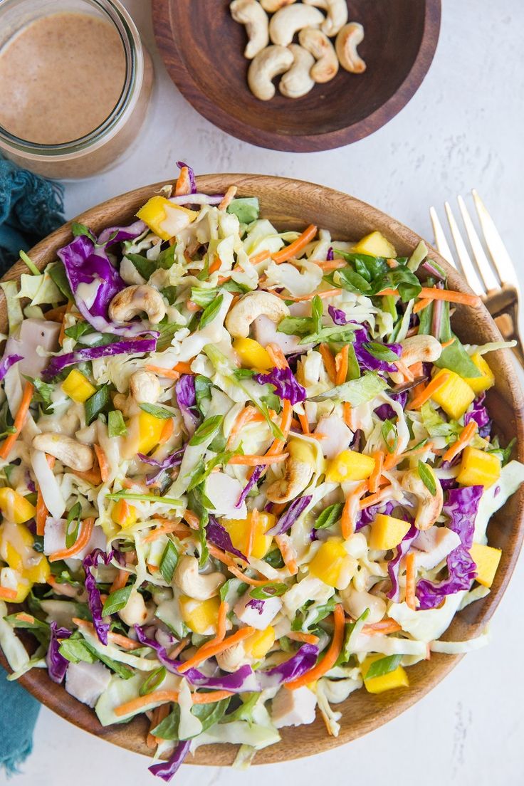 a salad in a wooden bowl next to two spoons and a jar of dressing