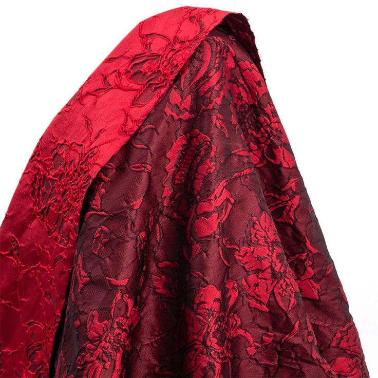 a red and black cloak with floral designs on it's back, draped over a white background