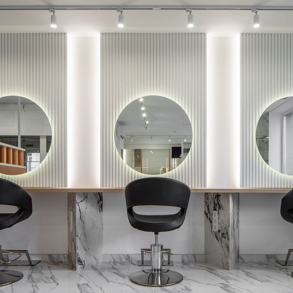 three mirrors are on the wall above two chairs in front of them, and one mirror is illuminated by lights