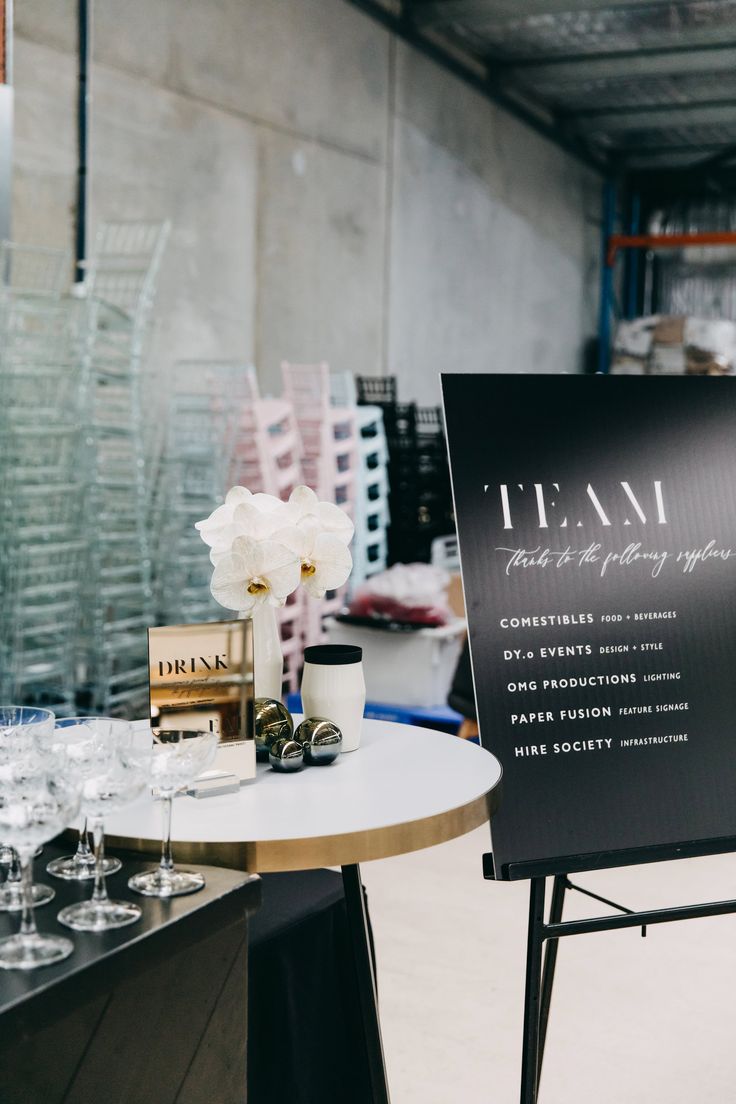 a sign that is sitting on top of a table with wine glasses in front of it