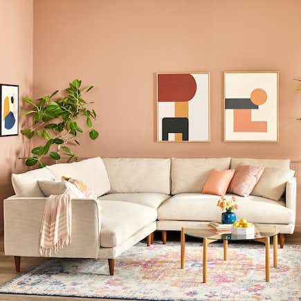 a living room filled with furniture and decor on top of a wooden floor next to a pink wall