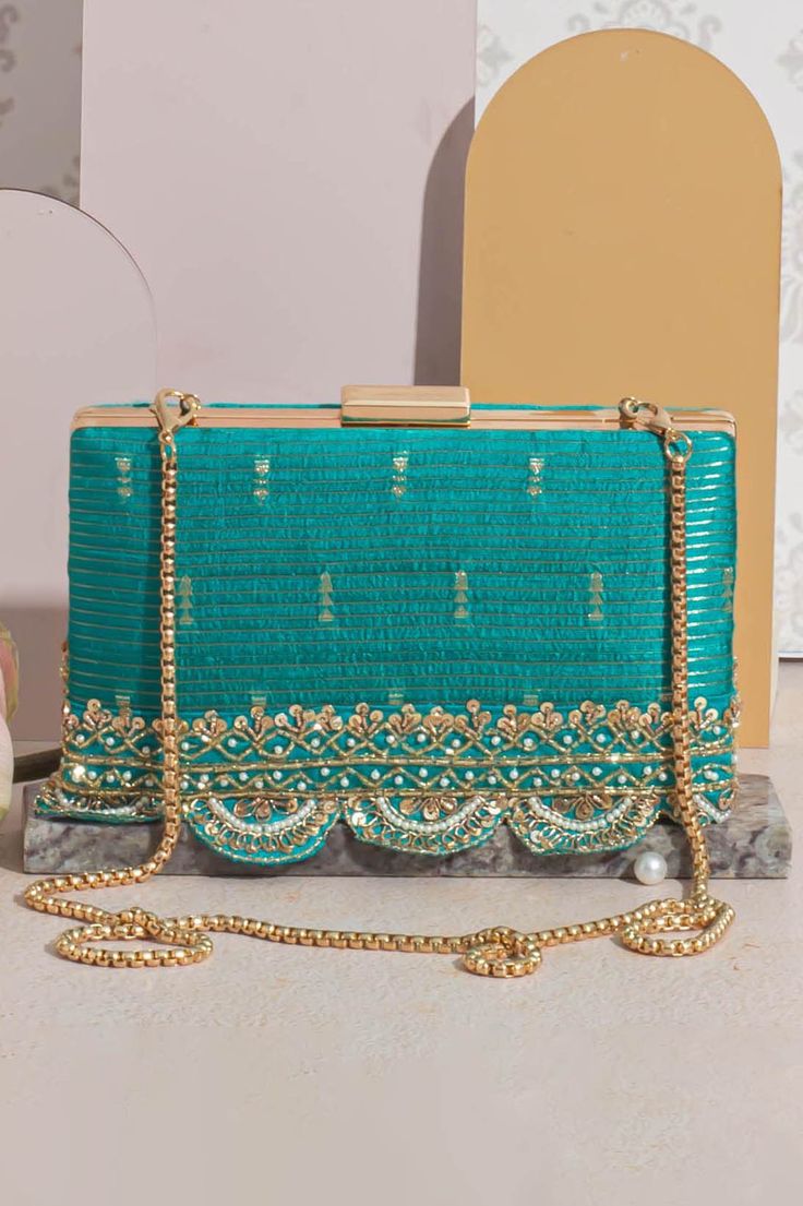 "Introducing Tari, a collection of exquisite raw silk potlis and clutches. Comes in an array of vibrant colors including regal purple, pink, mehndi green, warm mustard, and turquoise. The potli and the clutches are adorned with a delicate handcrafted embroidered border. The richness of material, captivating colors, and intricate details are an homage to South India. Perfect for all occasions, weddings, functions, and festive celebrations. Color: Turquoise Embroidered front and back. Dimensions (LxB): 7.75\"x4.5\" (19.7 cm X 11.4 cm) Handle length: 47\" (120 cm) Handle drop: 23\" (58 cm) Material: Embroidered pure silk, tissue inner lining, gold embroidered border lace, poly satin lining, gold metal clutch frame, gold metal sling. Features: metal lock closure, detachable metal sling." Elegant Diwali Raw Silk Embroidered Fabric, Elegant Embroidered Fabric With Gota Work For Diwali, Elegant Diwali Embroidered Fabric With Gota Work, Elegant Embroidered Fabric For Diwali, Elegant Embroidered Fabric For Diwali Festivities, Elegant Raw Silk Embroidered Fabric For Party, Celebration Tussar Silk Fabric With Zari Embroidery, Tussar Silk Fabric With Zari Work For Celebration, Festive Silk Thread Embroidered Fabric For Celebration