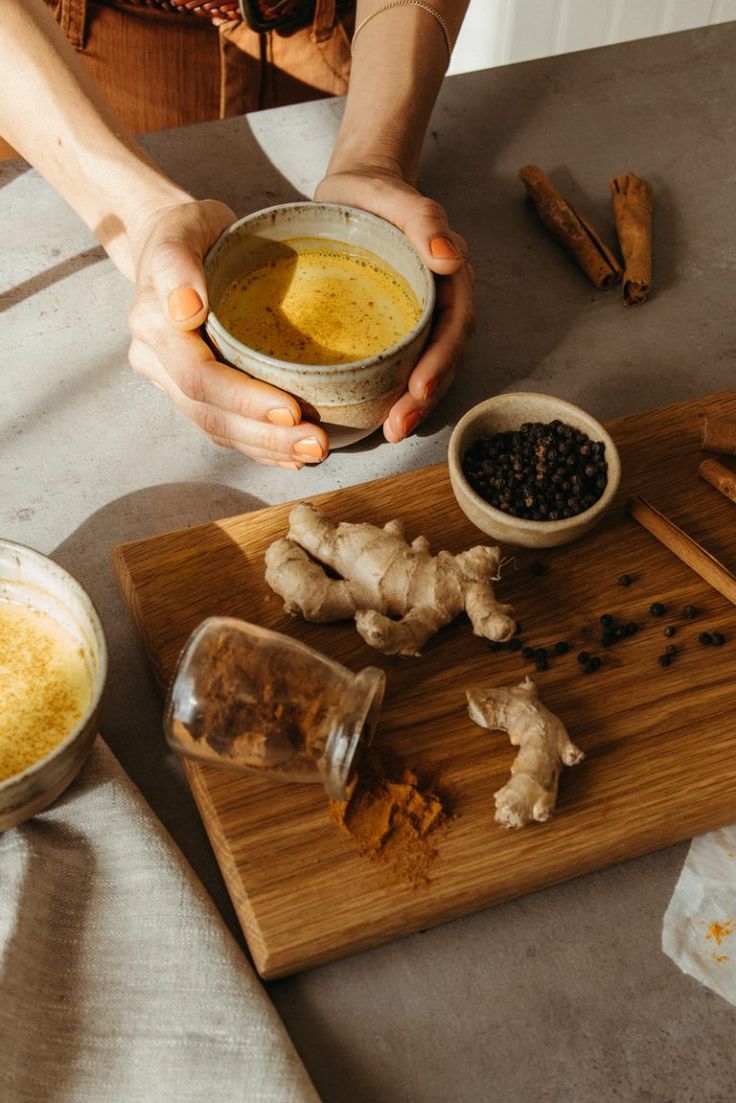 a person holding a bowl filled with food on top of a wooden cutting board next to other bowls