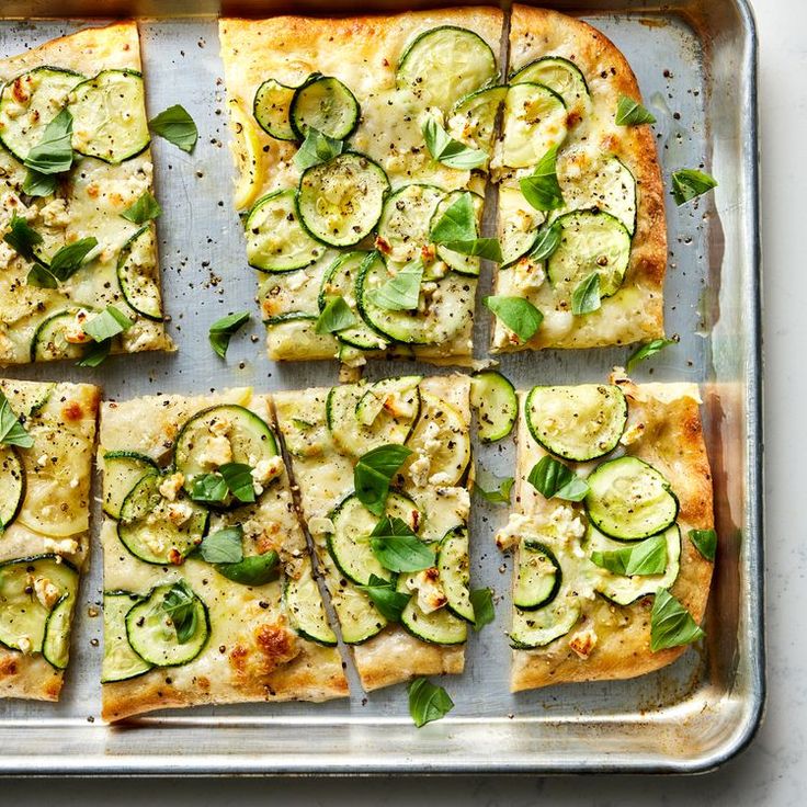 sliced zucchini pizza on a baking sheet with basil leaves and other toppings