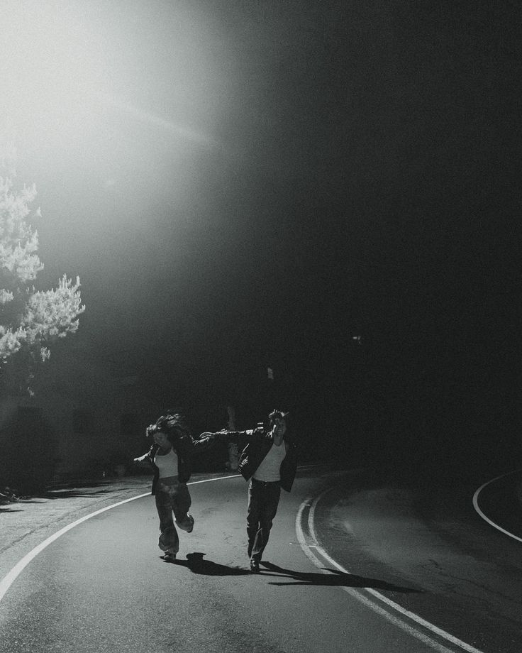 two people are walking down the street at night with their hands in each other's pockets