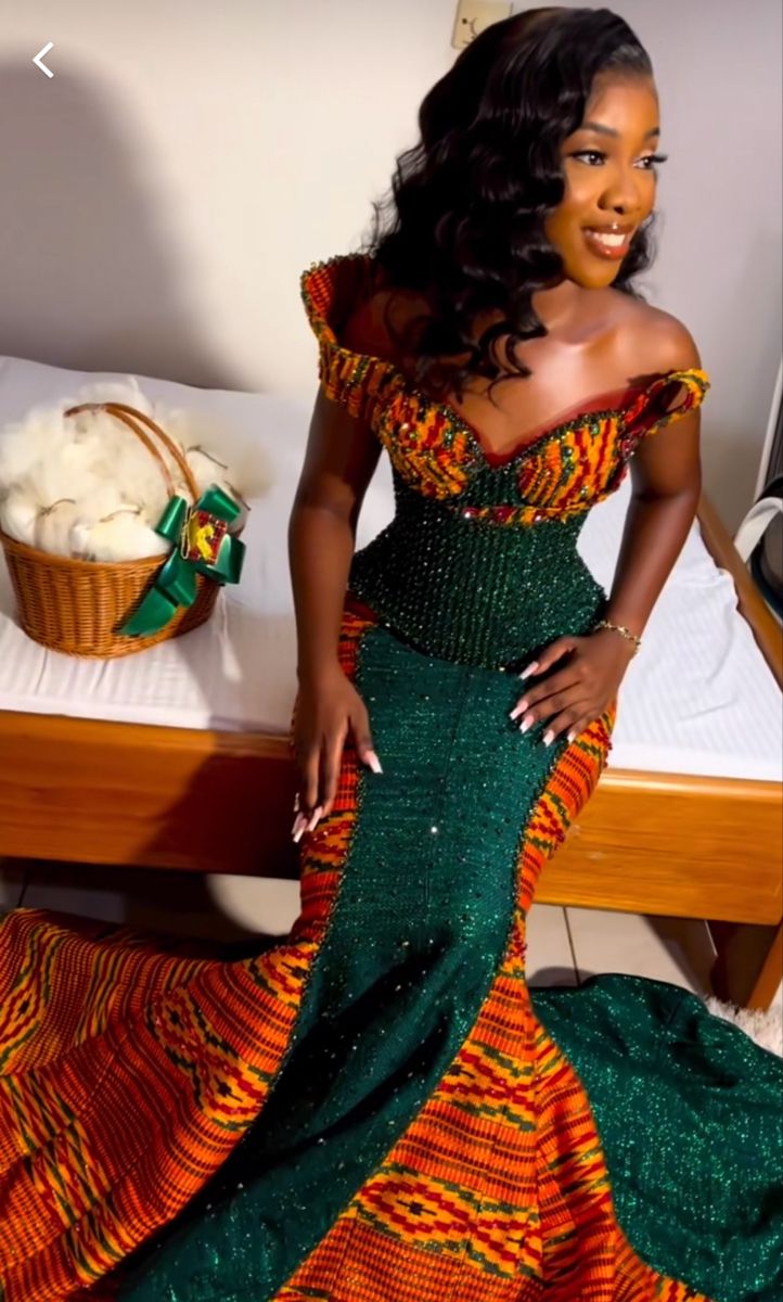 a woman in a green and orange dress standing next to a bed with a basket on it