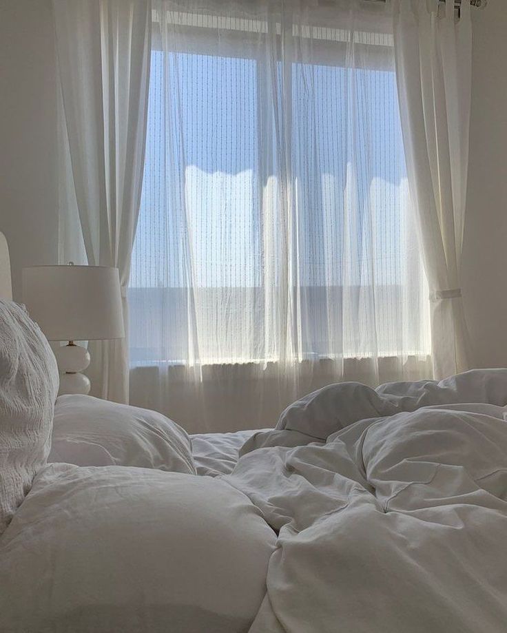 black and white photograph of an unmade bed in front of a window with sheer curtains