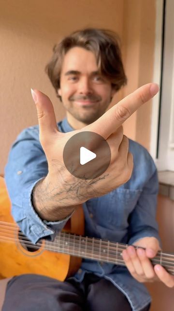 a man sitting down holding a guitar and making the peace sign with his hand while smiling at the camera