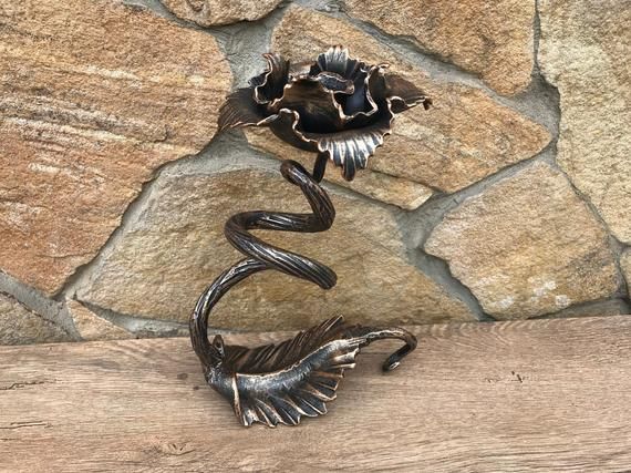 a metal flower sitting on top of a wooden table next to a stone wall and wood planks