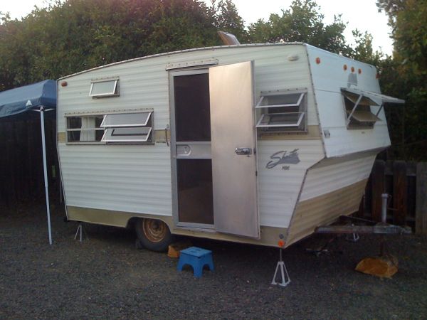 an old camper is parked next to a blue picnic table in the back yard