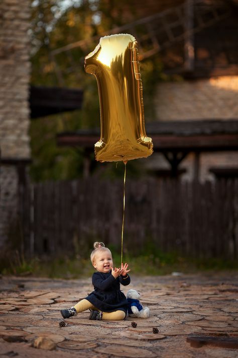 a baby sitting on the ground with a golden number balloon