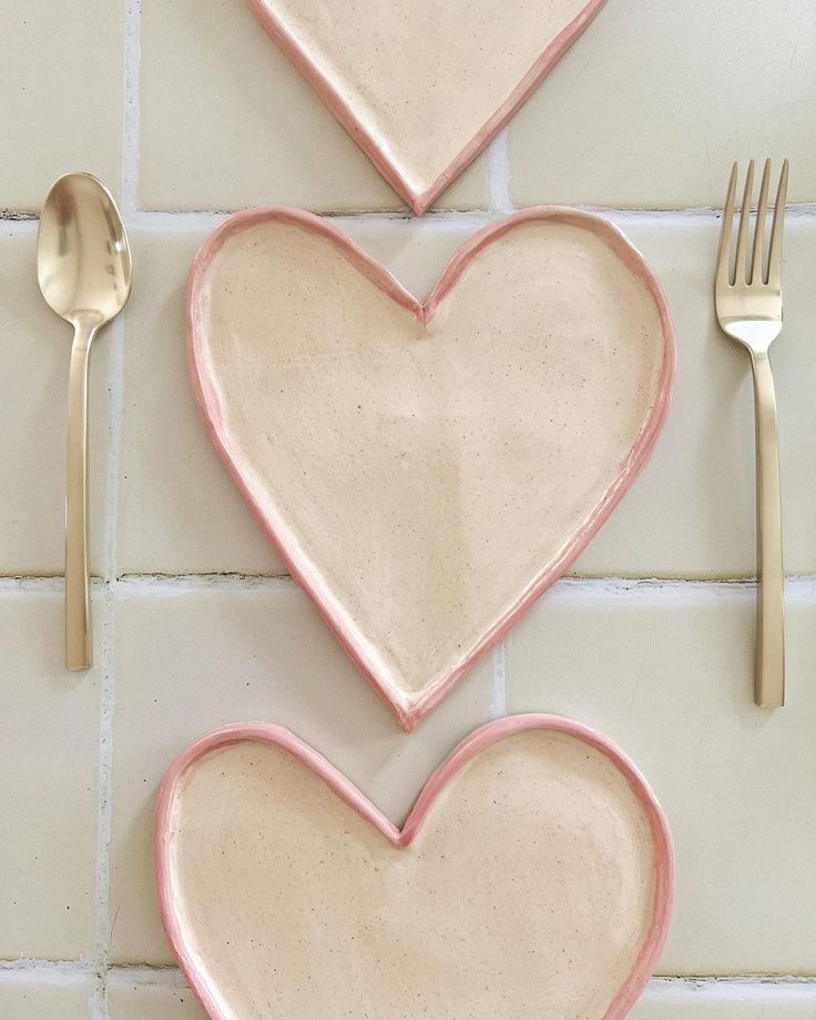 three heart shaped plates with forks and spoons next to each other on a tile wall