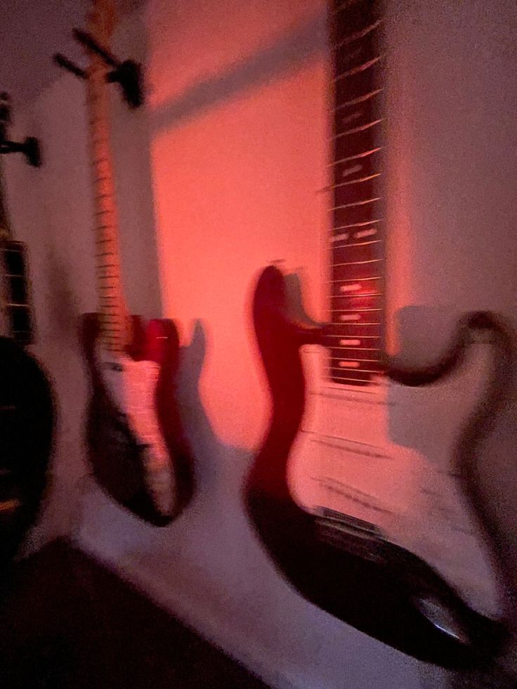 two guitars sitting on top of a white shelf next to each other in front of a red light