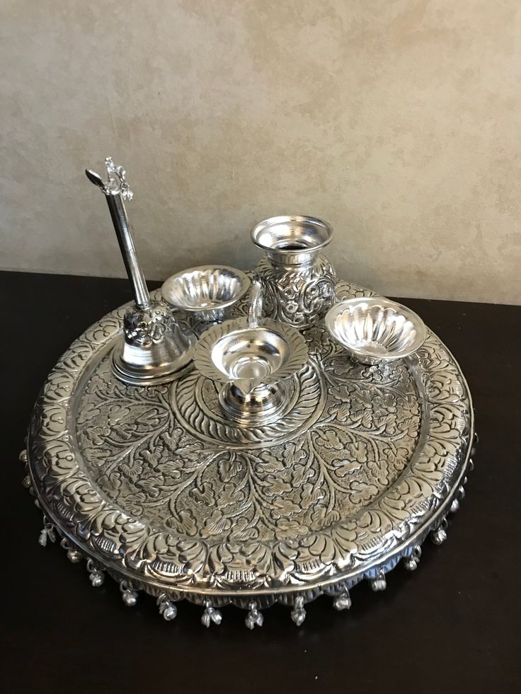 an ornate silver tray with four bowls and two spoons on the bottom, sitting on a black table