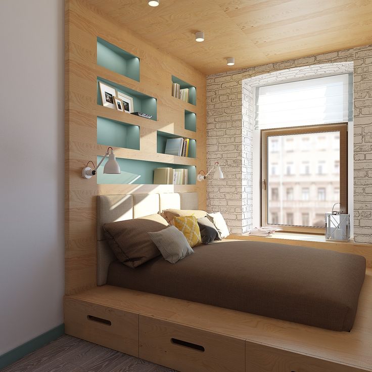 a bed sitting under a window next to a wooden shelf filled with books and pillows