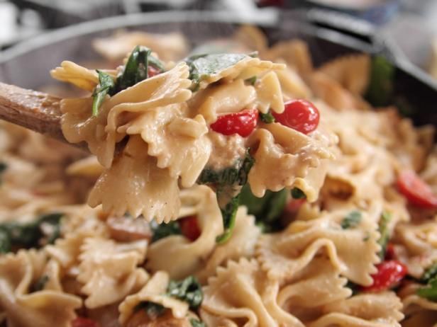 a spoon full of pasta with spinach, tomatoes and other toppings on it