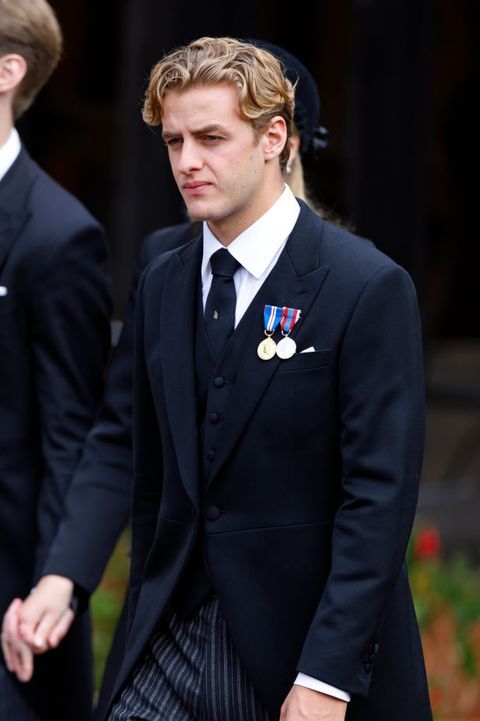 a man in a suit and tie walking down the street with another man behind him