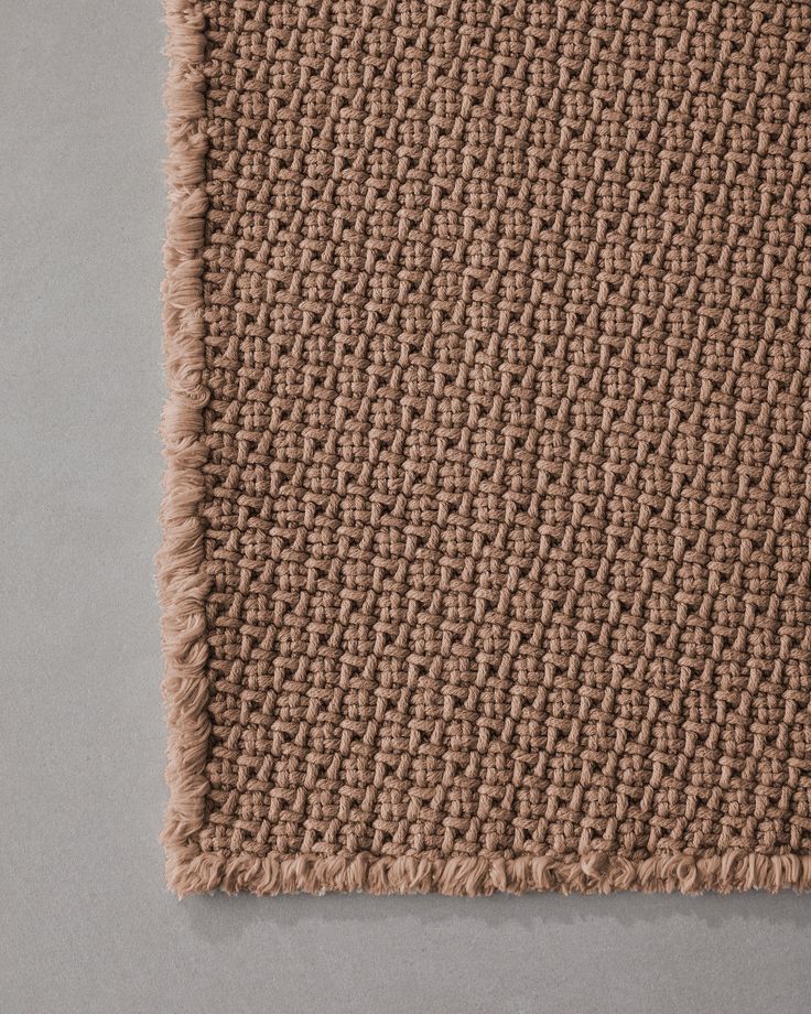 a brown rug with fringes on the bottom and side, laying on a gray surface