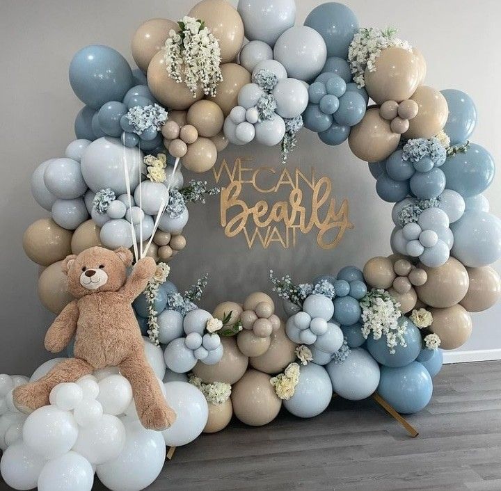 a teddy bear sitting in front of a balloon arch