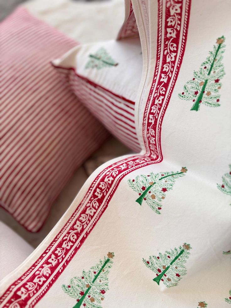 two pillows with christmas trees on them are sitting next to each other in front of a red and white striped pillow case