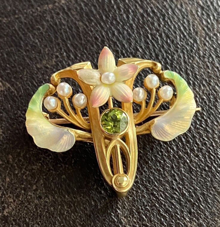 An enchanting Art Nouveau era flower pin by American maker Whiteside & Blank with iridescent enameling and a peridot center.  The soft pink petals remind us of cherry blossoms while the green enameled leaves look like samara seeds!  Wonderfully detailed with pearl accents.  The pin is stamped with the maker’s mark along with faded marks for 14K stamps. Metal: 14K Yellow Gold Weight: 6.1 grams Measurement: 1 inch long by 1.1 inches wide Markings: Maker’s mark Condition: In very good antique condition with some minor surface wear consistent with age.  One petal may have had the enamel touched up previously. Follow us on Instagram @alphaomegajewelry for the latest updates from our shop!  We have lots of fun there and add videos, highlights, and showcase our newest acquisitions. Art Nouveau Jewelry Vintage, Vintage Jewelry Art, Egyptian Revival, Pin Art, Art Nouveau Jewelry, Diamond Brooch, Bird Jewelry, Crown Jewels, Enamel Flower