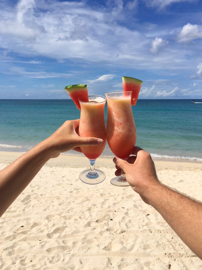 two people toasting with watermelon cocktails on the beach in front of the ocean