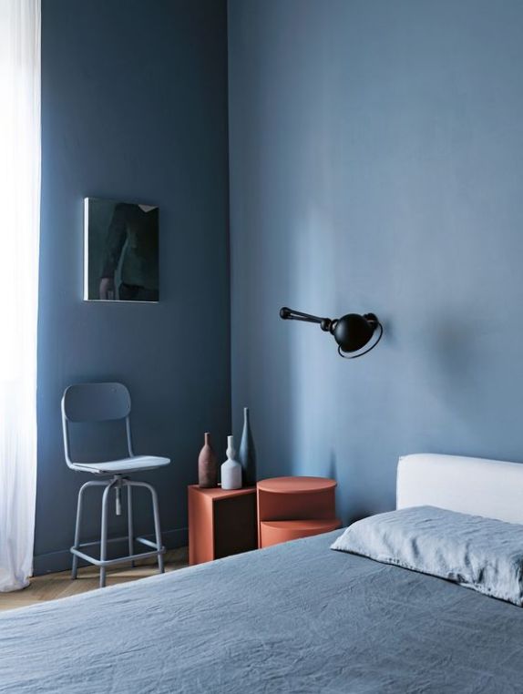 a bedroom with blue walls and white bedding, two stools and a mirror on the wall