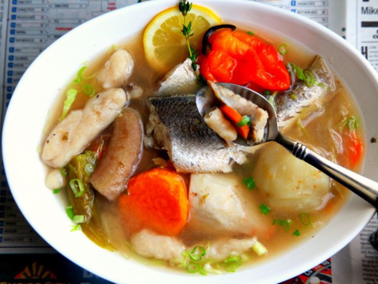 a white bowl filled with fish and vegetables on top of a table next to a newspaper