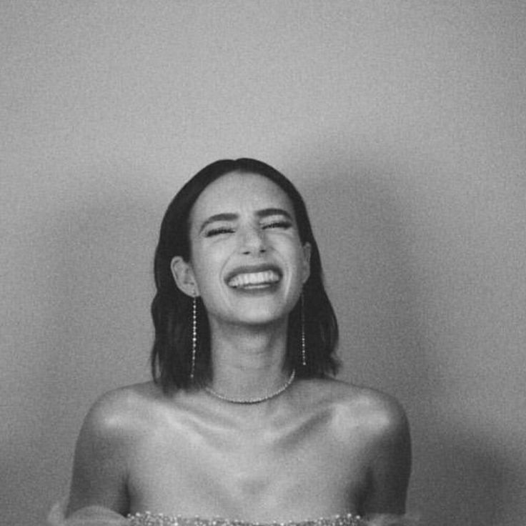 black and white photograph of a woman laughing in front of a mirror with her eyes closed