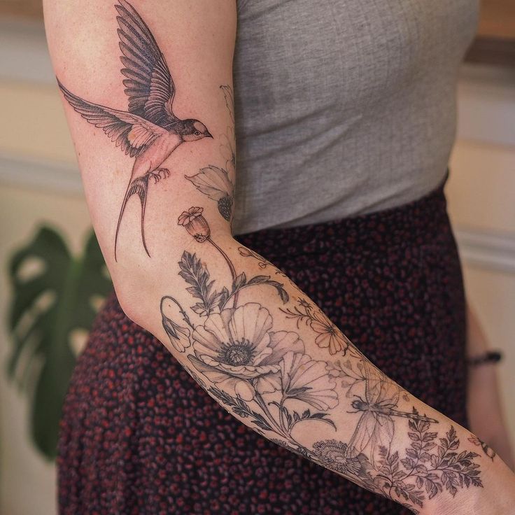 a woman's arm with a bird and flowers tattoo on the left side of her arm