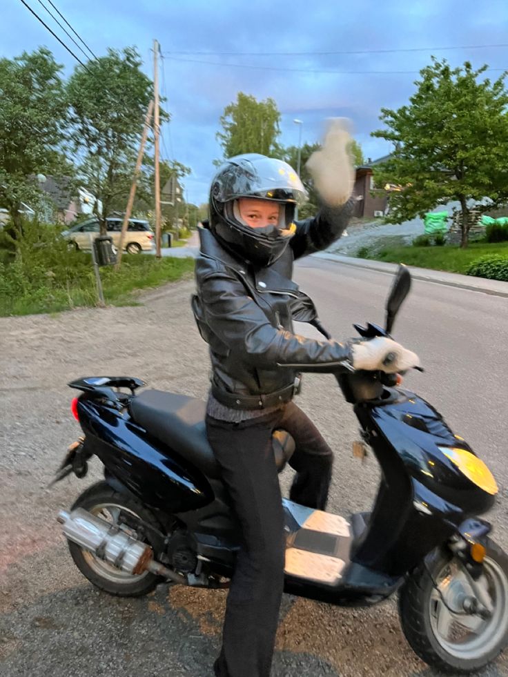 a person on a motor scooter wearing a helmet and gloves with one hand in the air