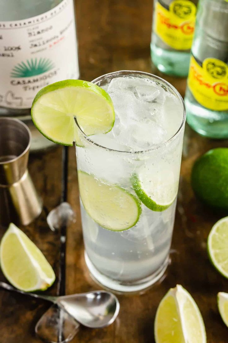 a glass filled with ice and limes next to two bottles of water on a table