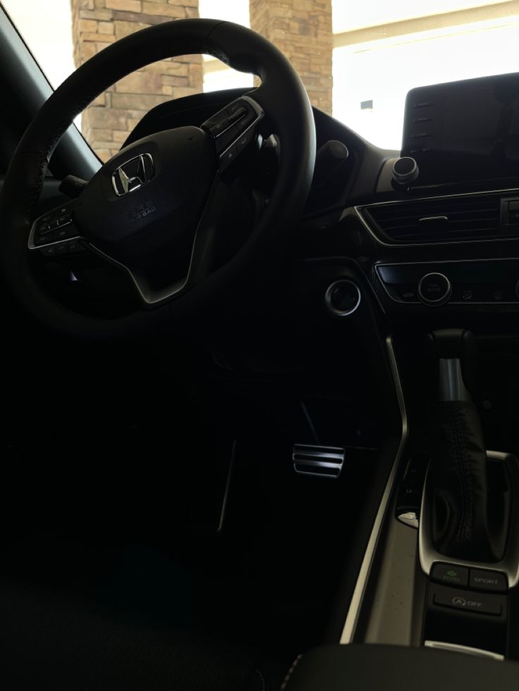 the inside of a car with its steering wheel and dash board showing, in front of a brick wall