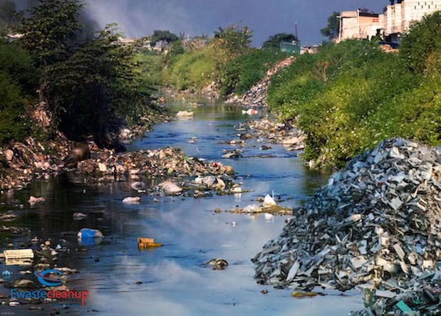 a river filled with lots of trash next to tall buildings and trees on the other side