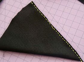 a piece of black fabric with yellow stitching next to a pink cutting mat and scissors