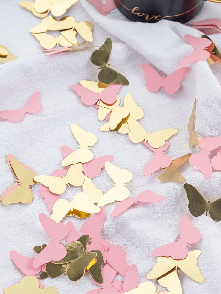 pink and gold butterfly confetti on a white tablecloth next to a bottle of wine