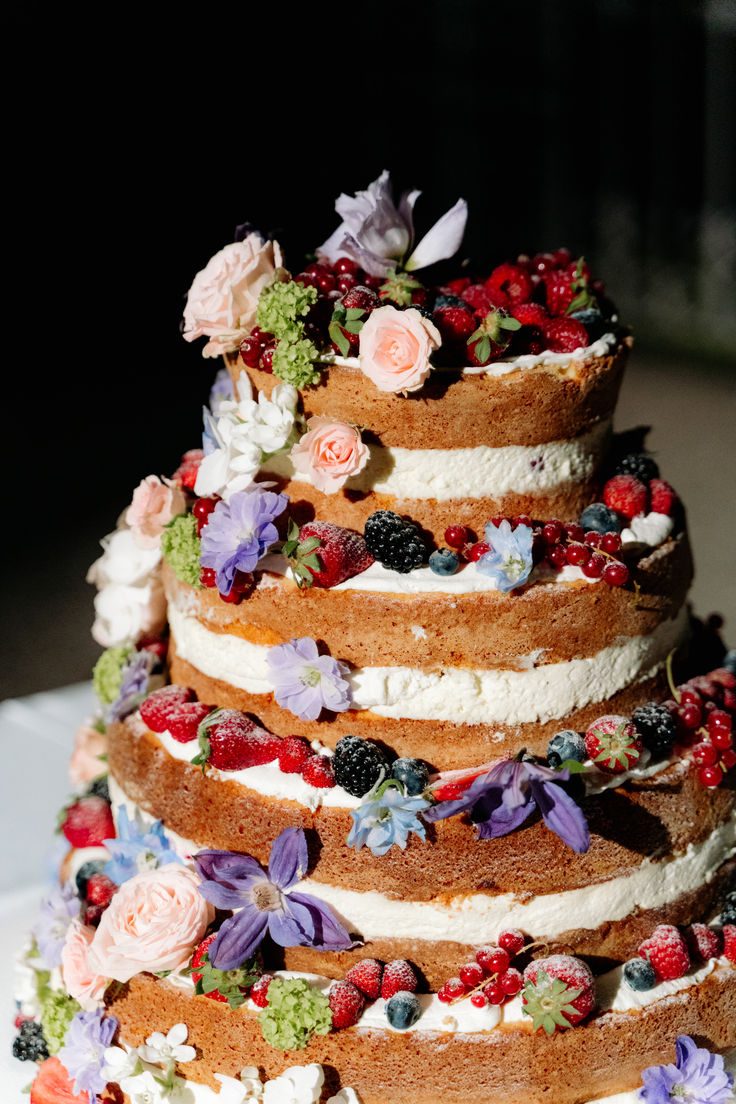 a multi layer cake with flowers and berries on it