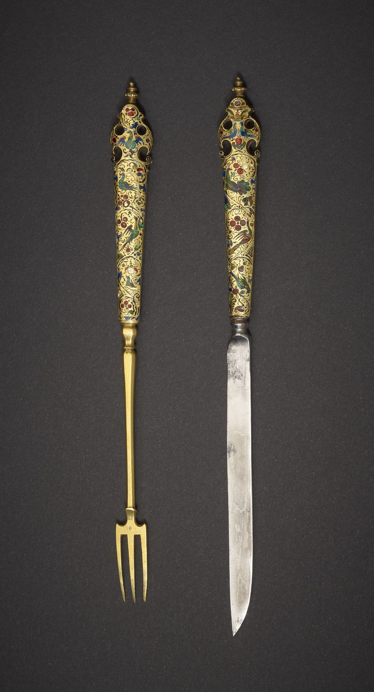 two knives and a fork on a black surface with gold trimmings in the shape of flowers