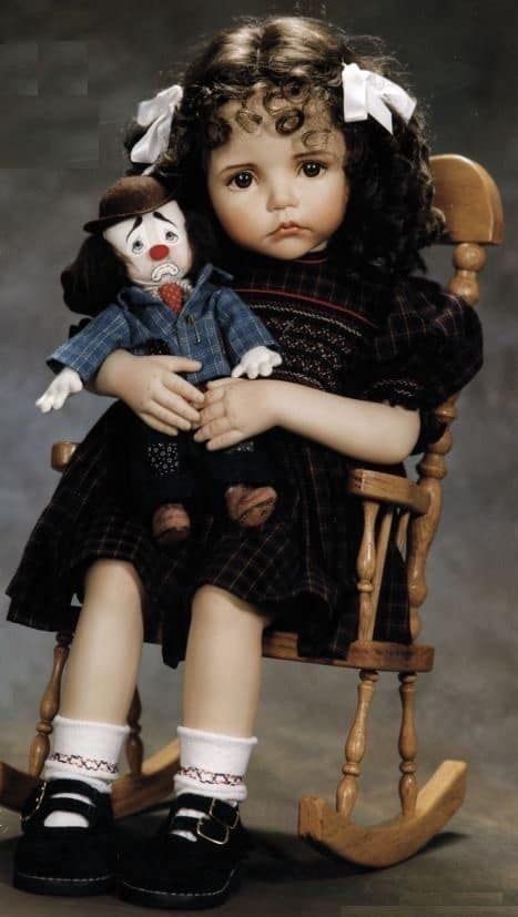 a doll sitting in a rocking chair holding a teddy bear and looking at the camera