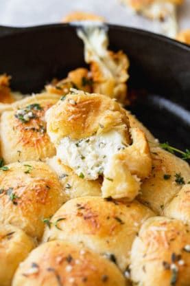 a skillet filled with rolls covered in cheese and herbs